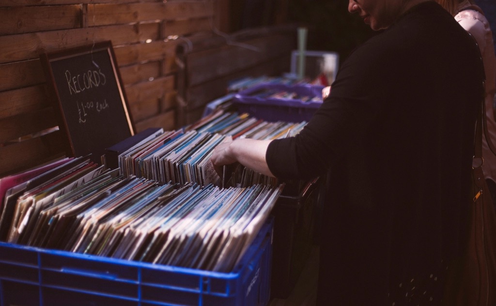 A crate-digger flicking through boxes of records at a Brighton market stall, chalkboard reading Records one pound each